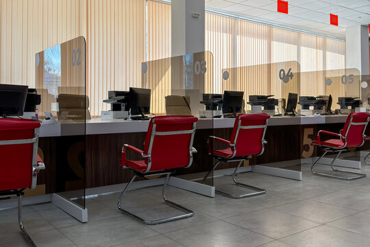 Modern bank interior featuring red chairs and glass partitions separating computer stations, with a spacious layout designed for customer service and efficient workflow in a well-lit environment
