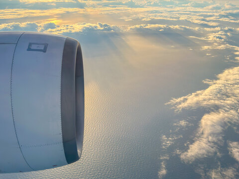 Airplane engine positioned near the window, capturing a view of the ocean and clouds below during sunset, with rays of sunlight breaking through the clouds in the background
