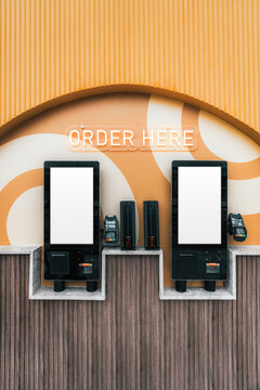 Two blank vertical touchscreens with card readers form a clean self-service ordering and payment terminal template beneath an illuminated Order Here sign in a modern restaurant