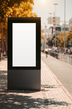 Blank vertical street display provides a clean urban advertising template, with spacious cycle path copy area and a distant cyclist silhouette softened by warm autumn bokeh