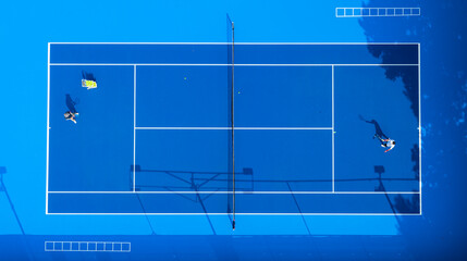 an empty blue hard tennis court scattered with yellow balls after a training session. The net, crisp white lines, and long shadows create a striking geometric background. © 晨啸 周