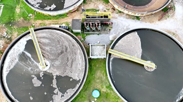 Wastewater treatment plant with circular clarifier tanks processing sewage. Urban sanitation and environmental infrastructure. Aerial drone view.