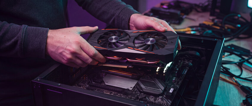 Graphics card installation in computer case with dual fan cooler above motherboard, illuminated by purple neon light for custom gaming pc build, hardware repair, and technology workshop