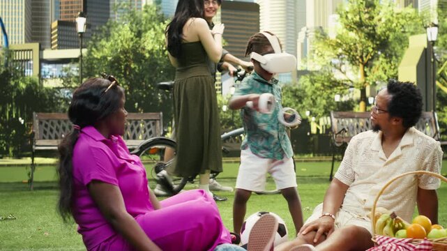 Boy wears virtual reality glasses and holds motion controllers near his parents on a picnic blanket in a city park during an immersive family VR activity.