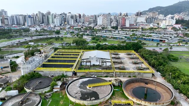 Wastewater treatment plant with circular clarifier tanks processing sewage. Urban sanitation and environmental infrastructure. Aerial drone view.