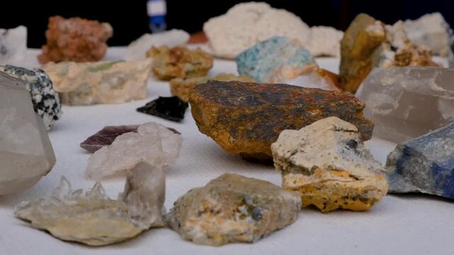 Close-up of rough gemstone rocks including aquamarine, pyrite, fluorite and quartz arranged on a display table. Collection of raw mineral specimens and natural crystals displayed