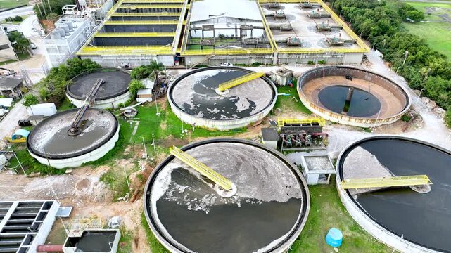 Wastewater treatment plant with circular clarifier tanks processing sewage. Urban sanitation and environmental infrastructure. Aerial drone view.