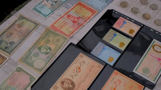 Antique paper money collection featuring historic South Asian banknotes, silver coins and first day covers on a table. Old rupee and taka currency notes with commemorative coins and postage stamps 