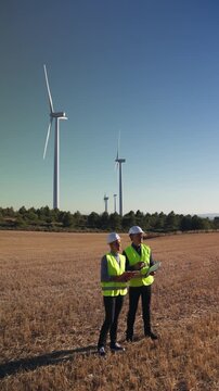 Engineers discussing plans near wind turbines in a field