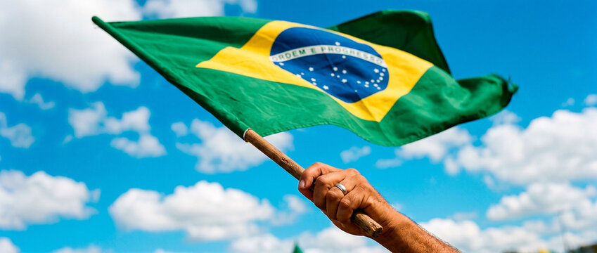 Brazilian man holding a waving Brazil flag against a blue sky. Patriotism, national pride, independence celebration, and Brazilian national holiday concept.