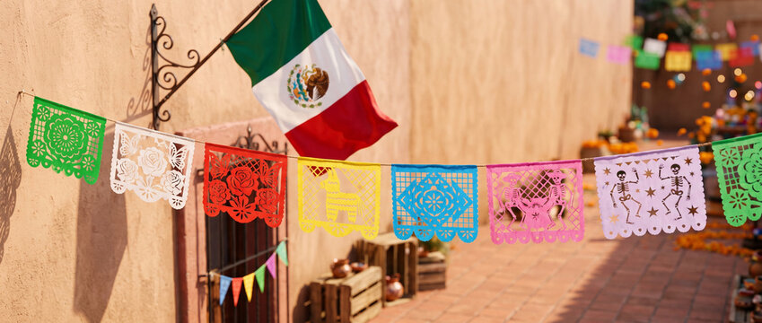 Mexican flag and colorful papel picado decorations outside a traditional courtyard for Independence Day celebration and Dia de los Muertos cultural festival