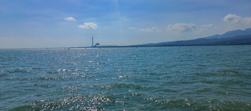 The beauty of the calm sea in a coastal area, set against a backdrop of boats and an industrial landscape.