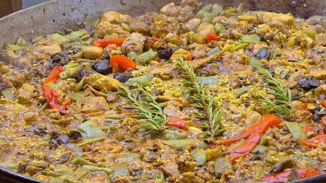 Close up shot of authentic Valencian paella cooking in a large pan with chicken, rabbit, green beans, red pepper and fresh rosemary.