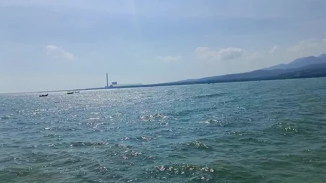 The beauty of the calm sea in a coastal area, set against a backdrop of boats and an industrial landscape.