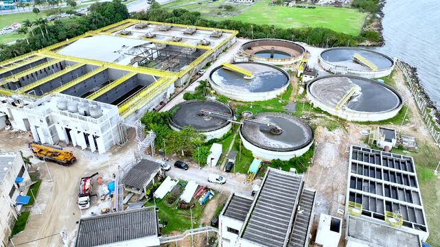 Wastewater treatment plant with circular clarifier tanks processing sewage. Urban sanitation and environmental infrastructure. Aerial drone view.