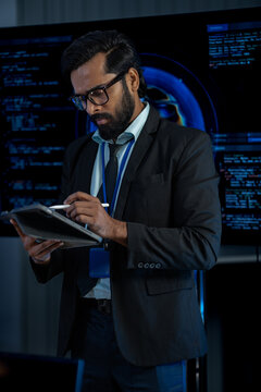 South Asian male and Black female software developers pair-program at dual monitors displaying network security algorithms at night.