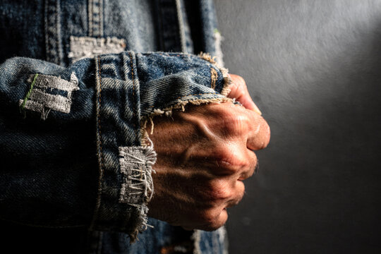 Weathered Hands Clenched in Frayed Denim Jacket Sleeve