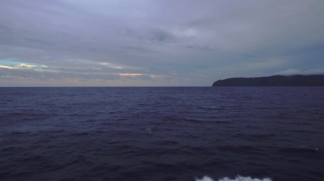 Passenger ferry sailing into the vast open ocean with a distant island fading on the horizon at dusk