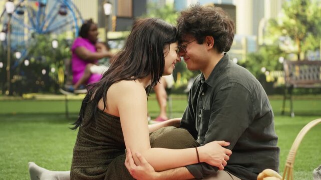 Couple touch foreheads with an intimate gaze while sitting together on a picnic blanket in a city park and showing romantic affection face to face.