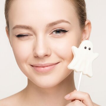 Young woman winking holding a cute ghost lollipop for Halloween celebration portrait