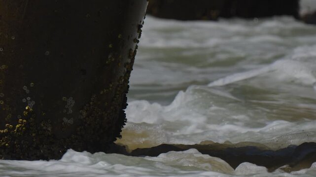 close up of waves breaking on pier pylons with barnacles
