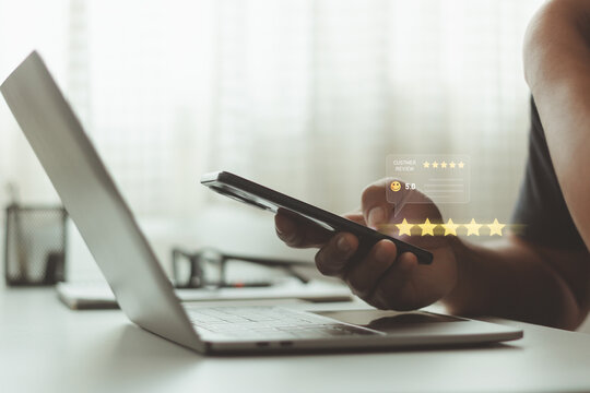 Customer giving online feedback with five star rating and smiley icon on smartphone, concept of customer satisfaction, user experience, service quality, online review , business reputation management.