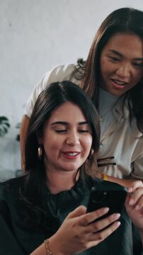 Salon, phone and woman with hairdresser for inspiration, hair treatment and talking at appointment. Happy, stylist and customer on cellphone for reference, internet and consulting for hairstyle
