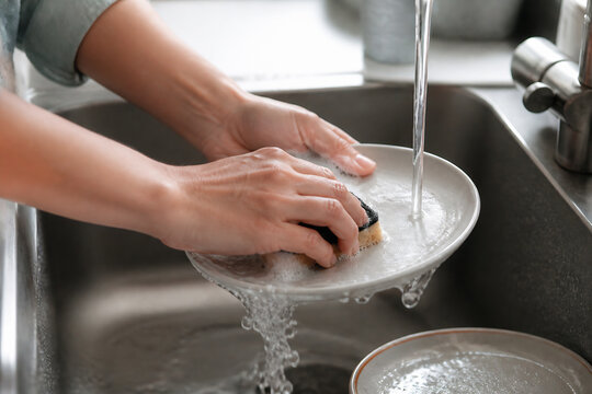 A person is washing dishes in a kitchen sink with running water.