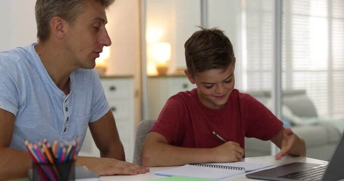 Father helping his son with homework at white table indoors
