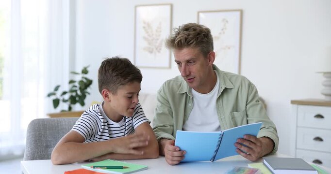 Smiling father with notepad helping his son with homework at white table indoors