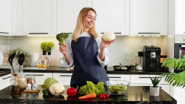 Middle-aged woman holds broccoli and cauliflower in kitchen promoting keto diet and healthy grocery haul for weight loss. Young girl learns low carb meal prep from home cooking vlog and keeps smile.