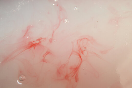 drops of red ink dissolve and spread artistically on the surface of the cloudy white liquid