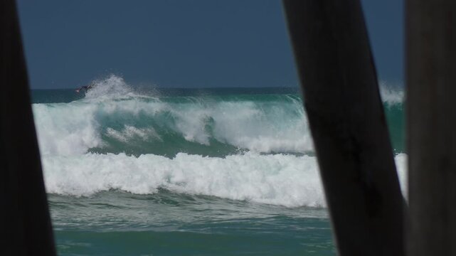 Surfers riding waves in between pylons of the pier