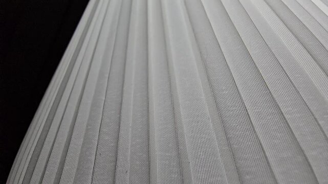 Close-up abstract shot of a white pleated material or lampshade with soft diagonal lines and clean minimalist textures.
