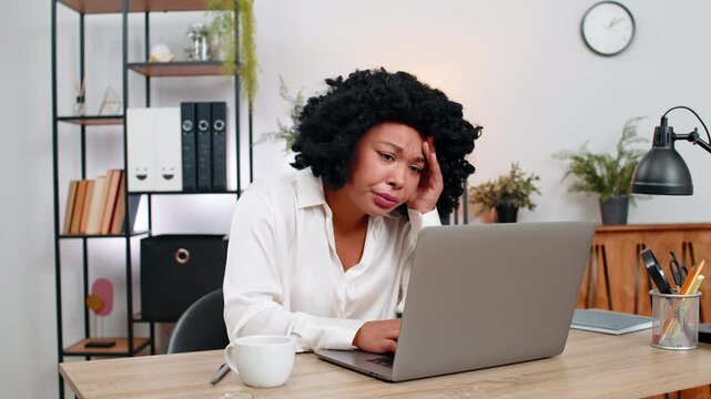 African American businesswoman at home office frowns at laptop upset by game defeat fail, rejection email. Freelancer girl at table sighs plans recovery seeking motivation and new goals after setback