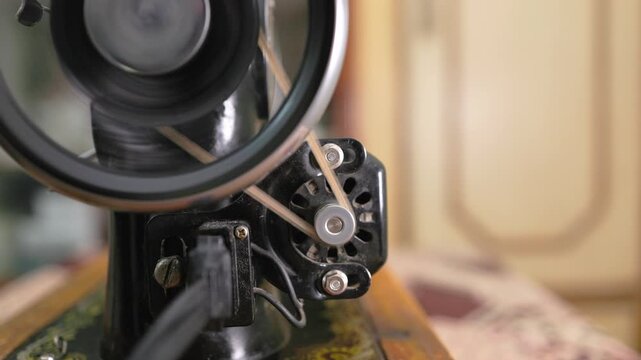 Macro shot of a black old sewing machine motor turning the balance wheel with a toothed belt, Retro tailoring equipment operating with shallow depth of field