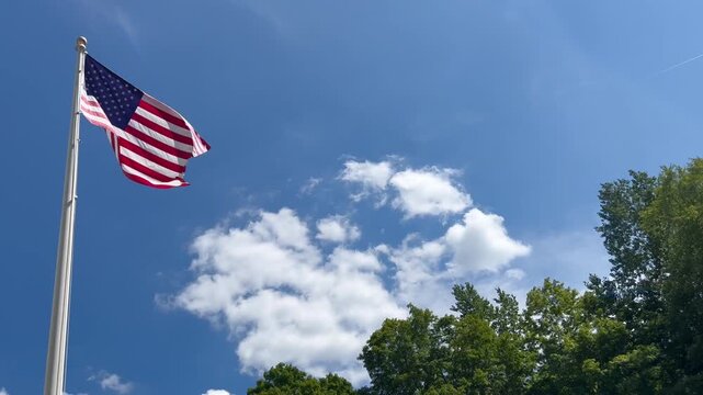 American flag flying on flagpole under blue sky with clouds