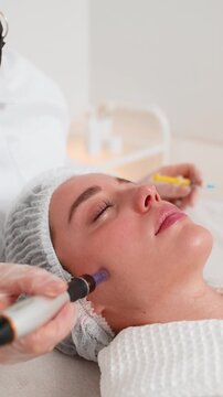 Caucasian woman girl undergoes facial rejuvenation using dermapen microneedling technique. Cosmetologist performs fractional mesotherapy procedure in beauty clinic to improve skin texture and health