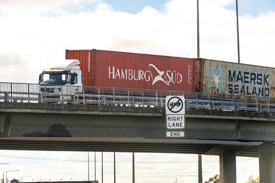 A semi-trailer truck hauling Hamburg S&uuml;d and Maersk Sealand shipping containers along an elevated overpass, past a "No Trucks Right Lane End" regulatory sign in Melbourne Australia. 
