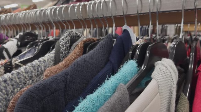 Close-up view of a clothing rack in a used clothing store, displaying a variety of sweaters and garments in different colors and textures, highlighting the selection available for shoppers