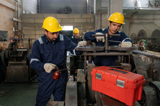 Technician wearing hardhat lubricating and adjusting machinery gears in industrial factory.