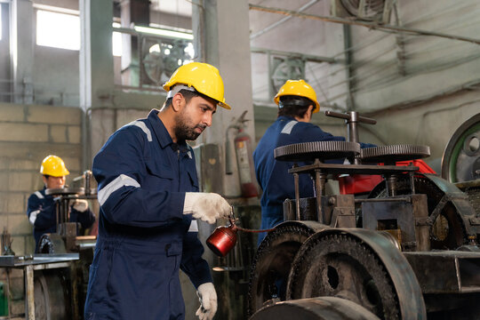 Technician wearing hardhat lubricating and adjusting machinery gears in industrial factory.