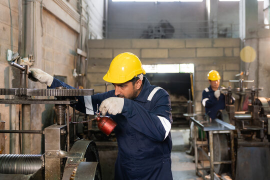 Technician wearing hardhat lubricating and adjusting machinery gears in industrial factory.