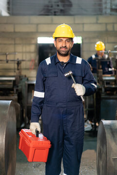 Vertical portrait of confident technician smiling while holding wrench and toolbox in industrial factory.
