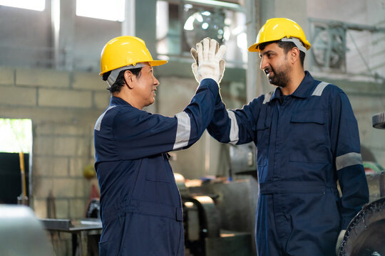 Engineers wearing hardhats giving high five celebrating successful teamwork in industrial factory.