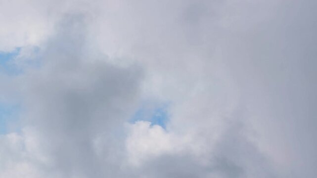 Timelapse of thick grey clouds rolling across the summer sky. Patches of blue open and close between them. Daylight shifts as the cover thickens and thins. A natural sky background with copy space.