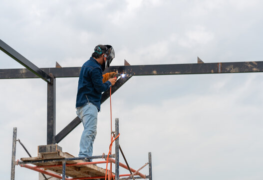 Professional welder working on high metal frame structure during building construction site work.