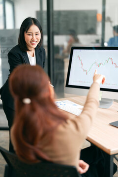 Asian Business Woman Smiling While Colleague Points at Stock Market Chart on Computer