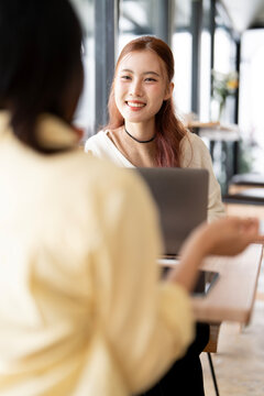 Asian Business Woman Smiling and Listening to Colleague During Meeting in Cafe