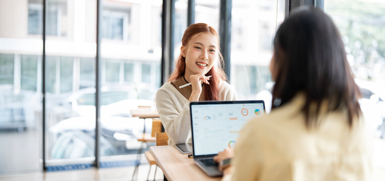 Asian Business Women Working on Laptop and Discussing Data in Modern Office Cafe